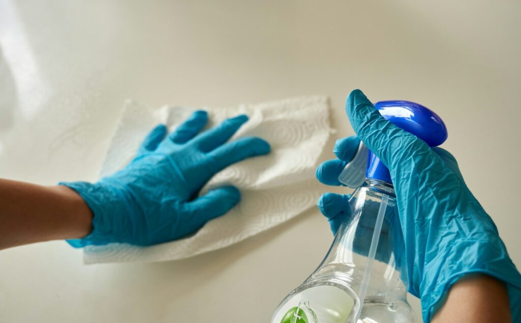 Gloved hands spraying sanitizer and wiping a white surface